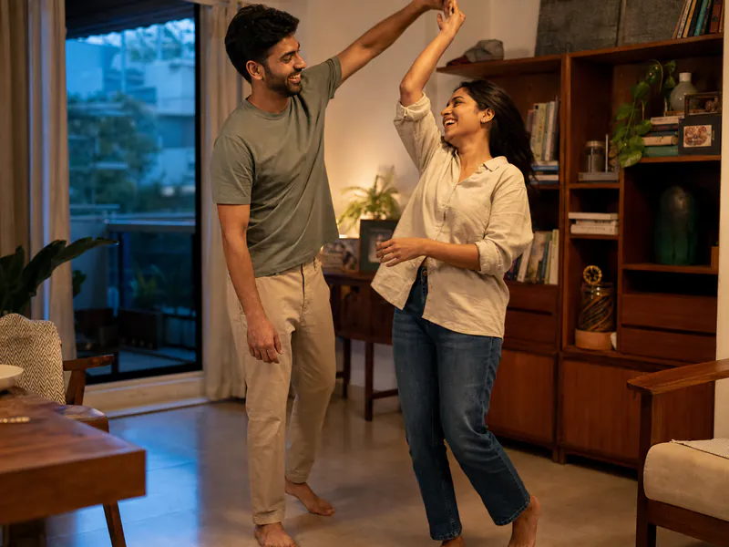 A young Indian couple dancing together in their sunlit home